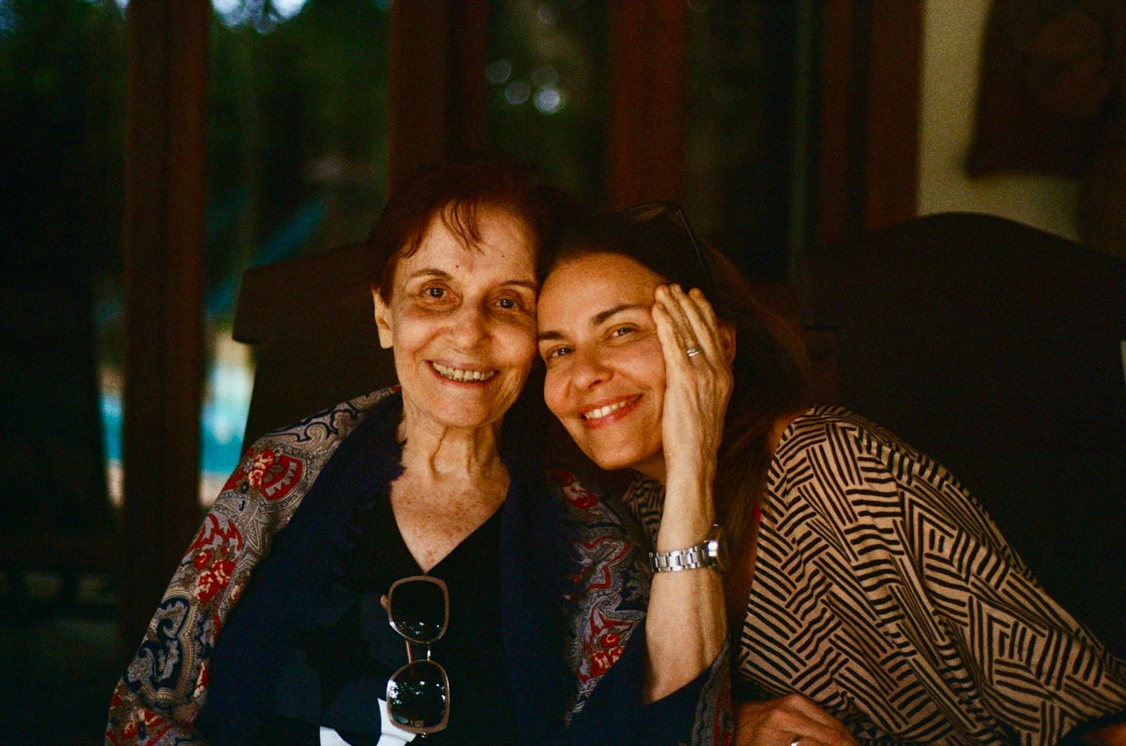 A mother and her adult daughter hugging and laughing outdoors